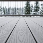 Composite deck boards in a modern Canadian outdoor space, photographed from a low angle with snow-dusted yard and evergreen trees in the background.