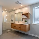 Modern bathroom with dual-flush toilet, low-flow rain showerhead, recessed LED lights, and ceiling exhaust fan, viewed from a corner at eye level; frosted window with light snowfall, clean tile, and warm wood vanity emphasize a modern, efficient design.