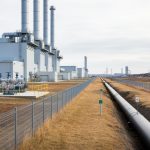 Wide view of a modern carbon capture and storage facility and fenced pipeline right-of-way in a Canadian landscape under an overcast sky.